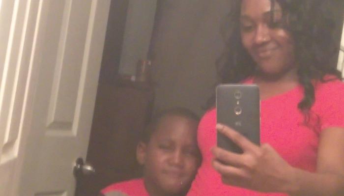 A smiling woman in a bright pink top taking a mirror selfie with a young boy next to her.