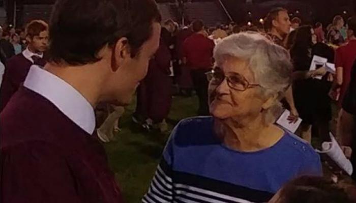An elderly woman smiling fondly at a young man in a burgundy sweater at a crowded evening event.