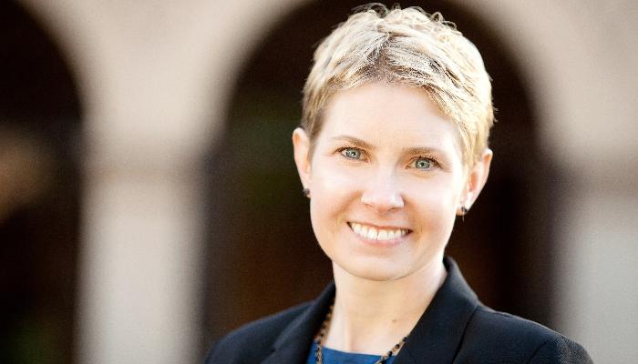 A smiling woman with short blonde hair and blue eyes wearing a black blazer.