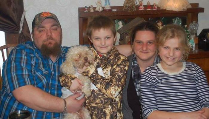A family of four with a father, mother, two children, and a small fluffy dog posing together indoors.
