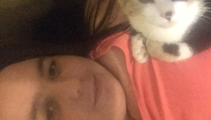 A smiling woman lying down with a calico cat resting on her chest.
