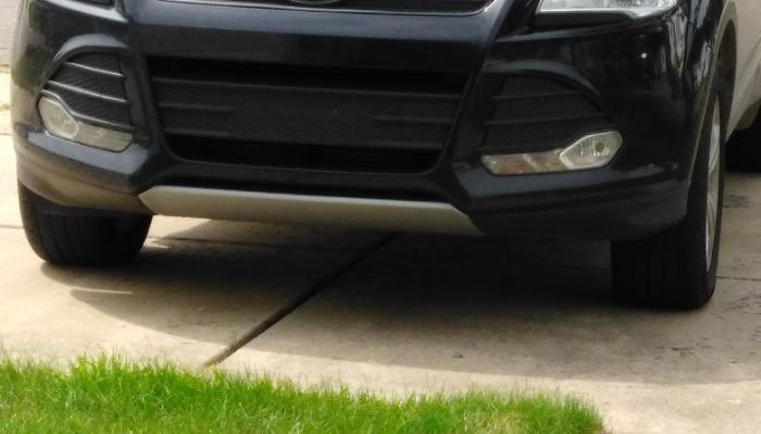 Front bumper, fog lights, and silver lower skid plate of a dark SUV parked on a concrete driveway.