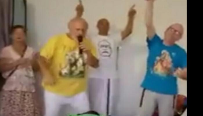 A group of people joyfully singing into a microphone and dancing with their arms raised.