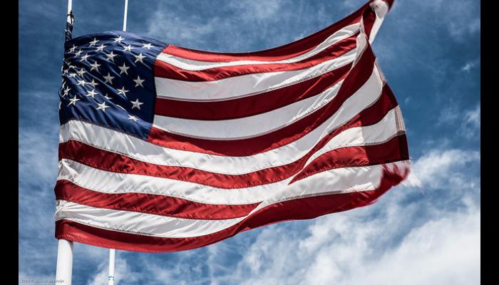 An American flag waving in the wind against a blue sky with light white clouds.