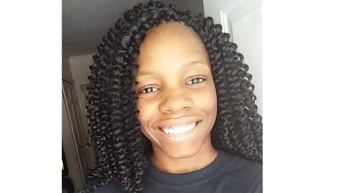 A smiling young Black woman with shoulder-length dark curly twists.