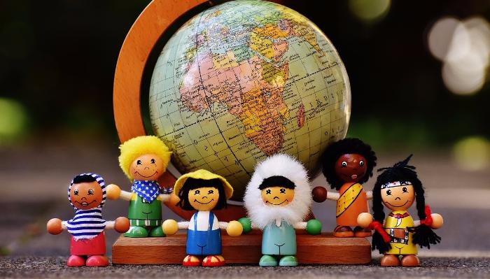 Six diverse wooden figures representing children from around the world stand in front of a desk globe.