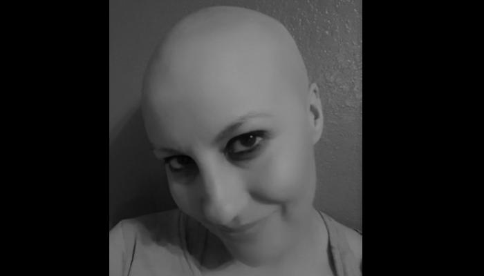 Close-up black and white portrait of a bald woman smiling softly at the camera.