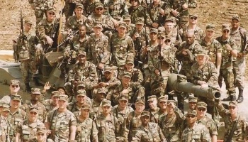 A large group of soldiers in camouflage uniforms posing together outdoors on a military vehicle.