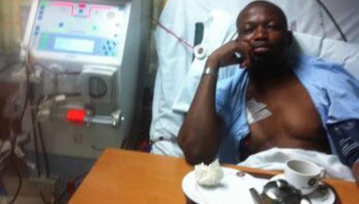 A man resting in a hospital bed next to a dialysis machine with a tray of tea in front of him.