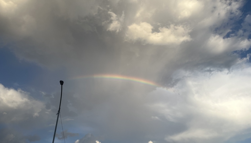 A rainbow arching across dramatic grey storm clouds with a tall silhouetted street lamp on the left.
