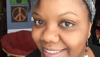 Close-up of a smiling Black woman wearing a patterned headwrap and dangling beaded earring.
