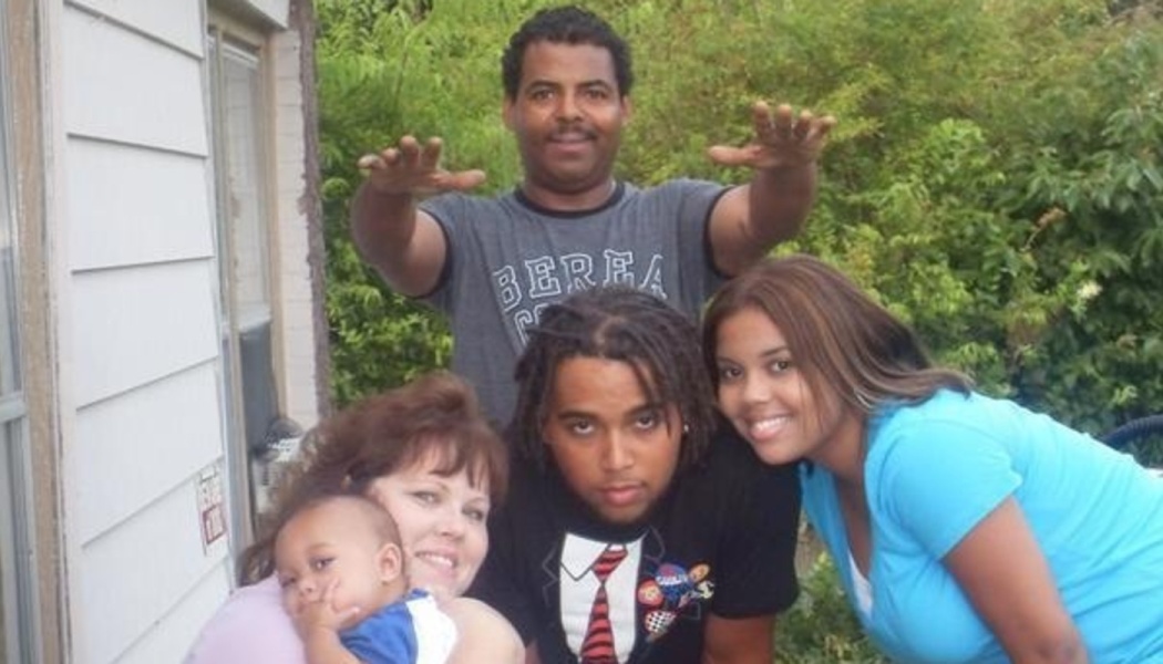 A smiling family of five, including parents, two young adults, and a baby, posing together outdoors.