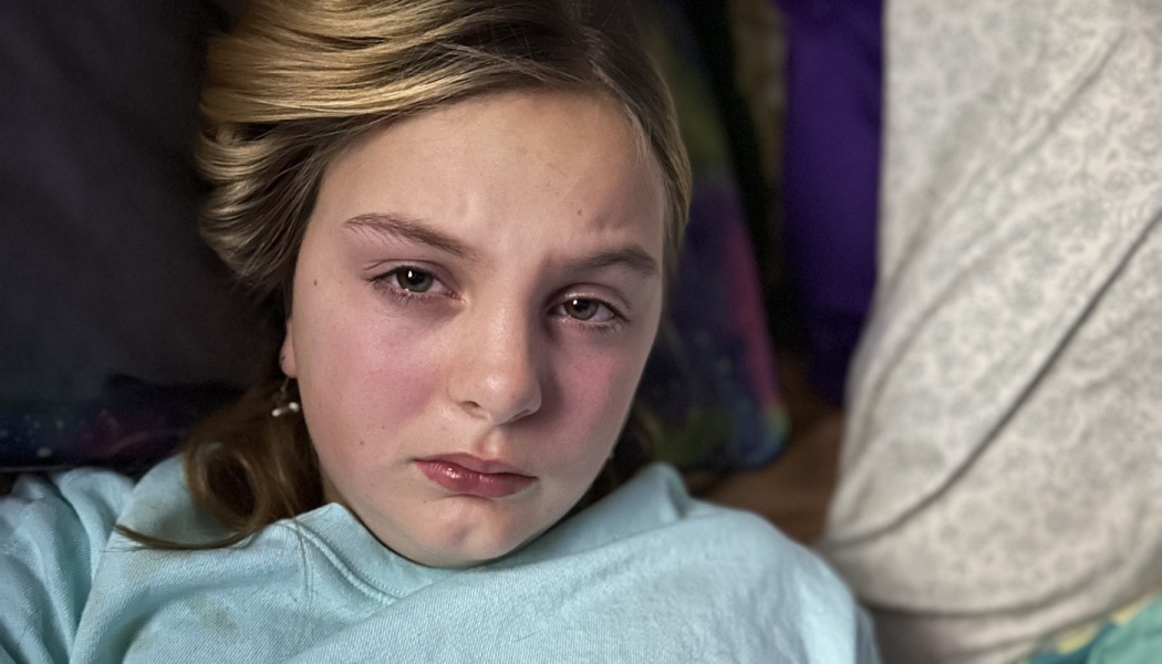 Close-up of a young blonde girl with teary, swollen eyes looking sad while lying down.
