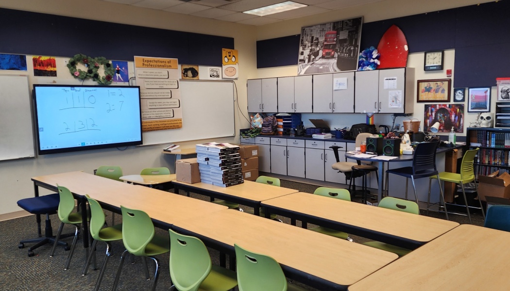 Empty classroom with student desks, lime green chairs, an interactive whiteboard, and stacks of textbooks.