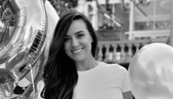 Black and white portrait of a smiling woman with long dark hair next to party balloons.
