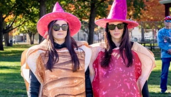 Two women wearing bright pink witch hats and peanut butter and jelly sandwich costumes in a park.