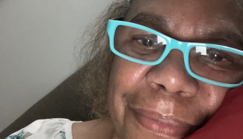 Close-up selfie of a woman with bright turquoise glasses smiling gently while resting.