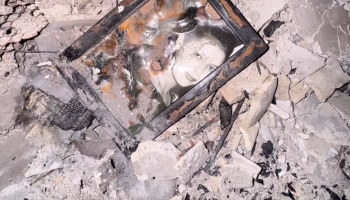 A fire-damaged framed portrait of a woman lying amidst concrete rubble and ash.