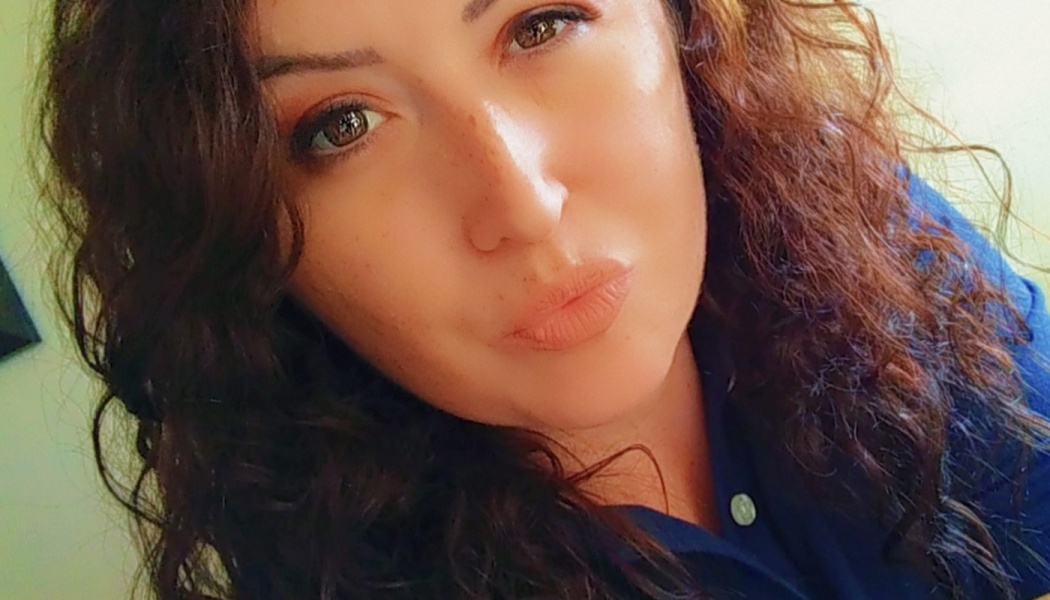 Close-up portrait of a woman with long dark curly hair and brown eyes looking at the camera.