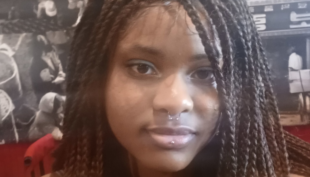 Close-up portrait of a young Black woman with long braided hair, a septum ring, and lip piercing.