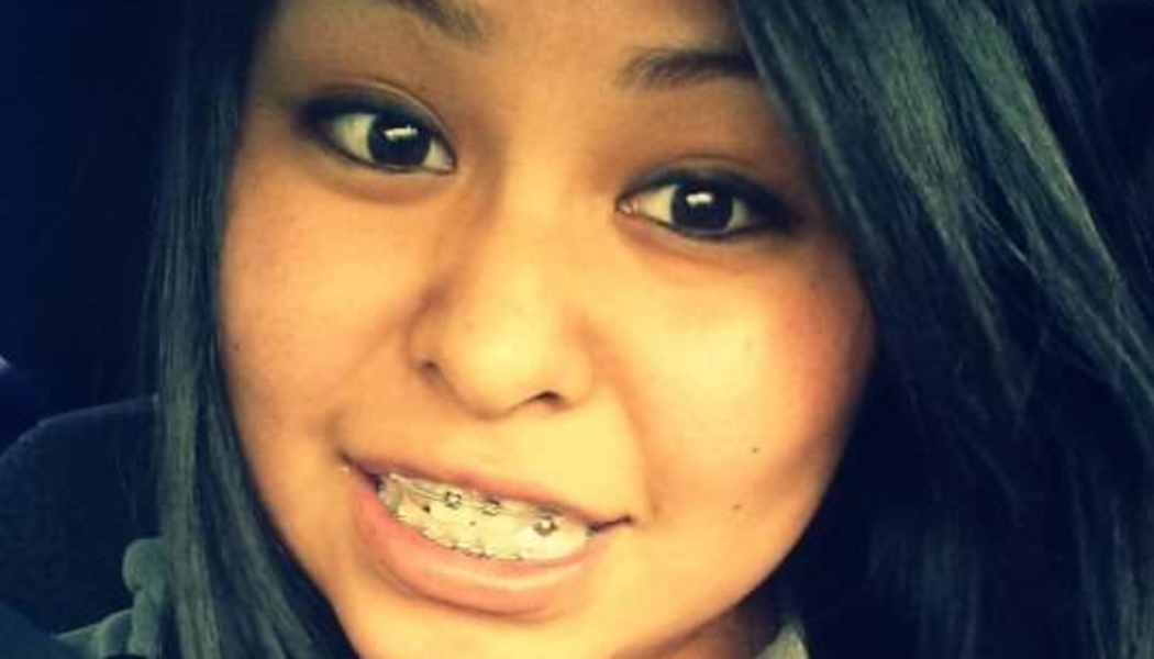 Close-up portrait of a young woman with long dark hair smiling and wearing braces.