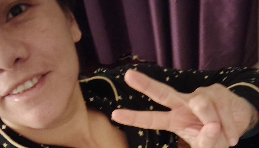 A smiling person making a peace sign gesture, wearing black pajamas with small gold stars.