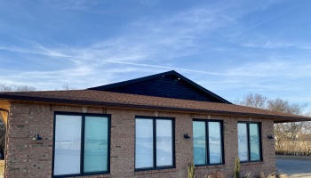 Exterior of a modern brick building with black-framed windows and a brown roof against a blue sky.