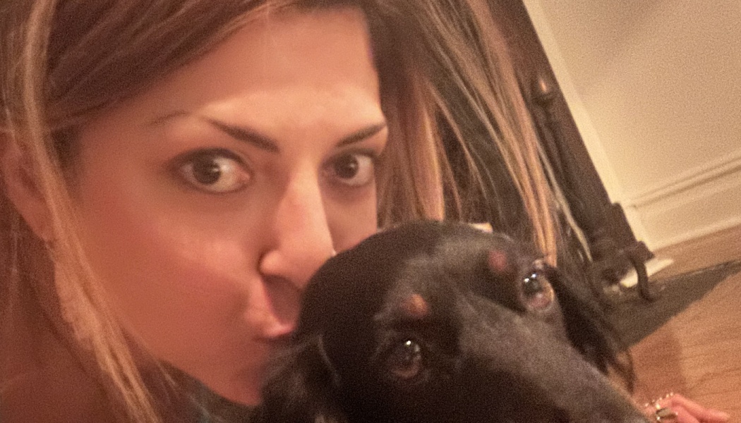 Close-up selfie of a woman kissing her small black and tan dog.