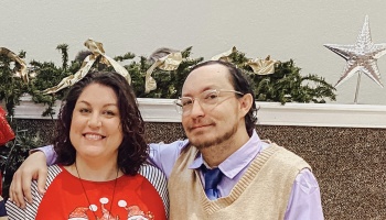 A smiling couple poses together warmly in front of festive holiday garland and a star decoration.