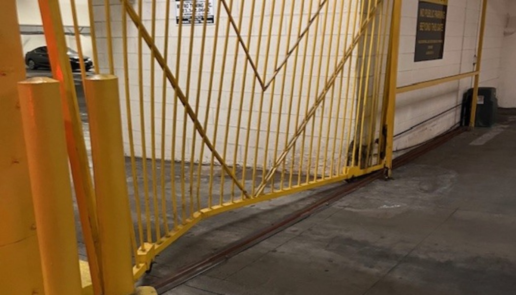 A broken and bent yellow metal security gate hanging off its track in a parking garage.