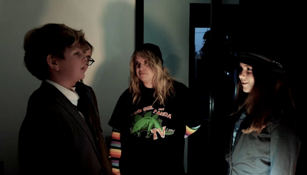 Four young actors gather in a dimly lit room, conversing during a scene.