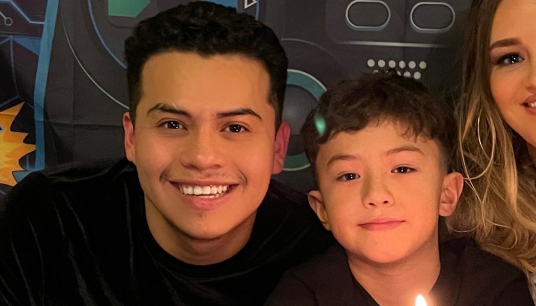 A smiling young man and a young boy posing together closely at a celebration.