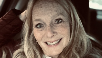 Close-up portrait of a smiling woman with long blonde hair and freckles.