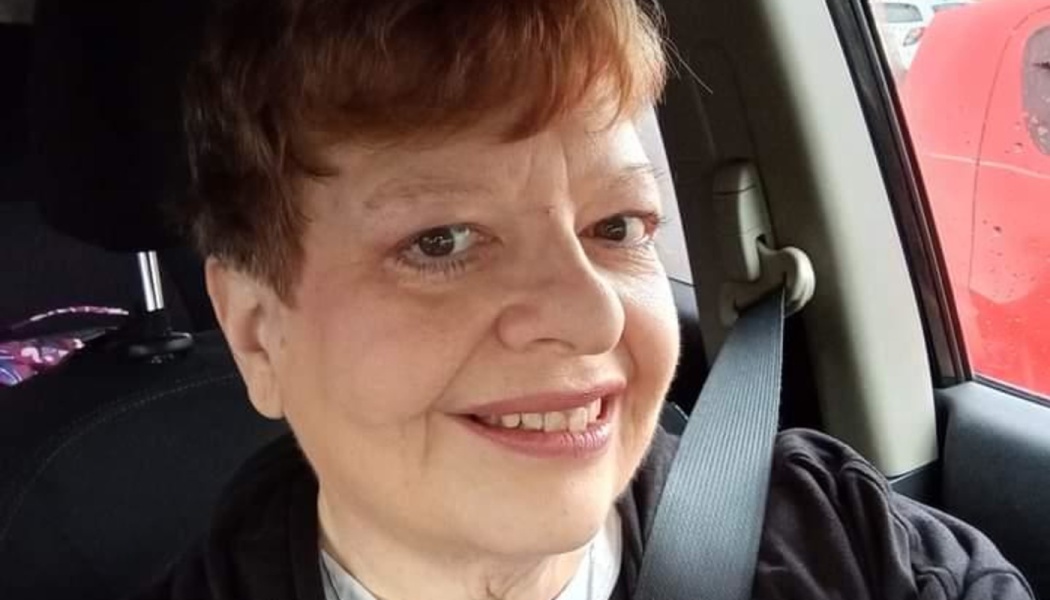 Close-up of a smiling woman with short auburn hair sitting inside a car wearing a seatbelt.