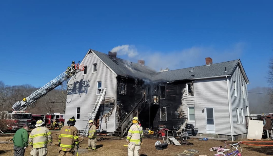 Firefighters and a ladder truck at a heavily charred, fire-damaged two-story house.