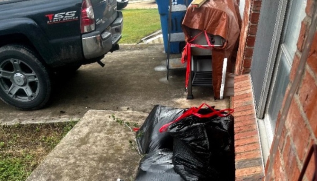 Black trash bags piled outside a brick home next to a parked pickup truck.