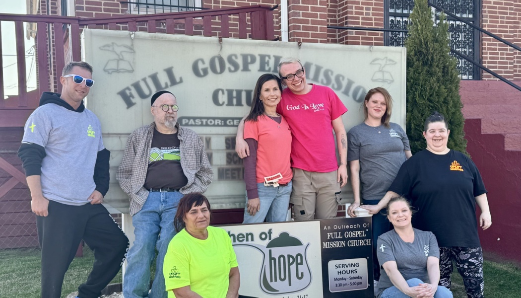 A group of volunteers smiling in front of the Full Gospel Mission Church and Kitchen of Hope signs.
