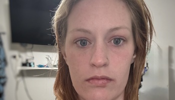 Close-up portrait of a woman with light hair, blue eyes, and a nose piercing looking directly at the camera.