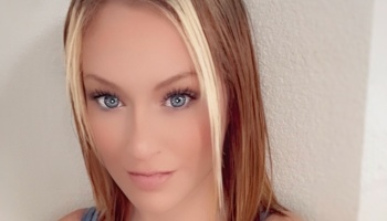 A young woman with striking blue eyes and blonde front highlights framing her light brown hair.