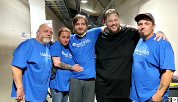 Musician Jelly Roll posing backstage with a family wearing blue Make-A-Wish t-shirts.