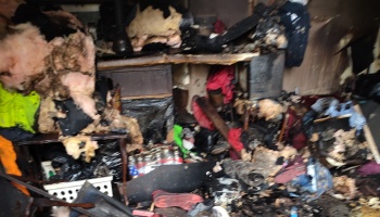 Heavily fire-damaged room filled with charred belongings, scorched furniture, and soot-covered debris.