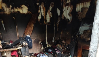 Severely fire-damaged room with heavily charred walls, exposed insulation, and burnt debris scattered on the floor.