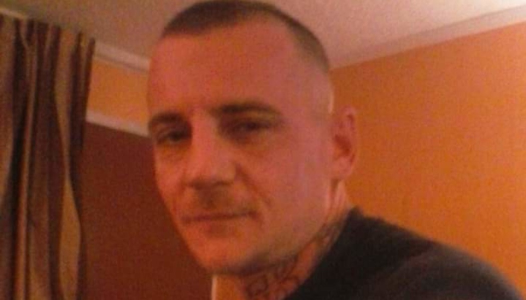 Close-up portrait of a man with short buzzed hair and neck tattoos.