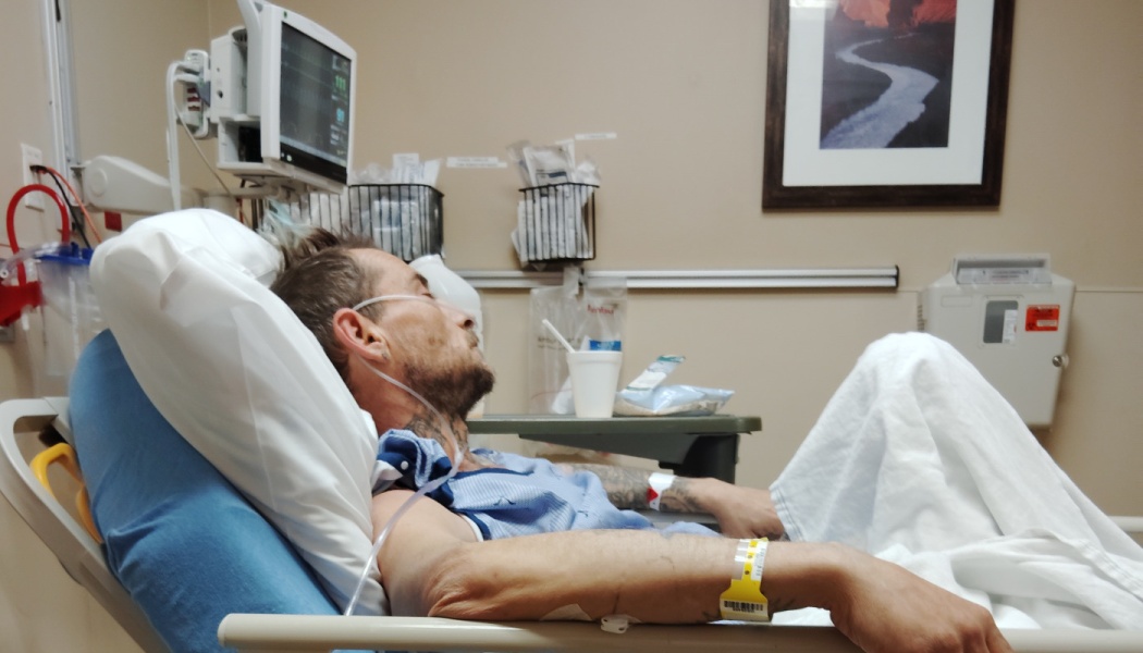 A male patient resting in a hospital bed with an oxygen cannula and medical monitors nearby.