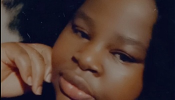 Close-up portrait of a young Black woman with voluminous dark hair resting her hand against her face.