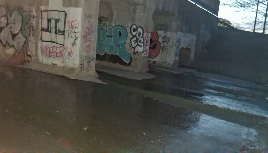 Colorful graffiti covers concrete pillars in a dim, wet urban underpass.