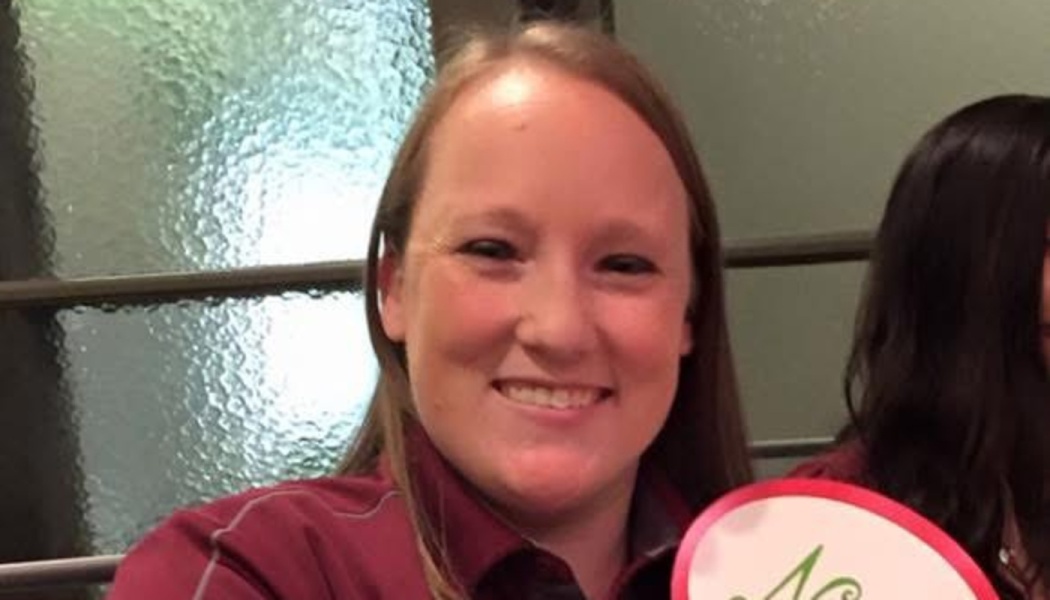 A smiling woman with light brown hair wearing a maroon shirt.