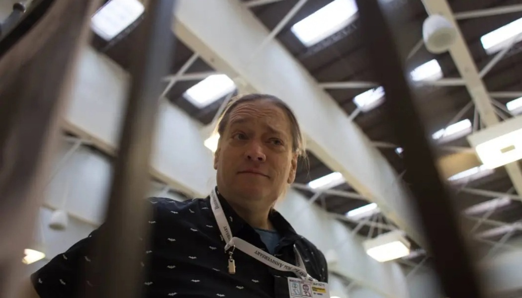 Low-angle view of a person wearing a bat-patterned shirt and lanyard, looking downward in a large skylit hall.
