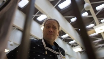 Low-angle view of a person wearing a bat-patterned shirt and lanyard, looking downward in a large skylit hall.
