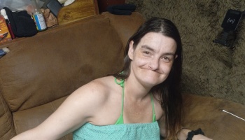 A smiling woman with long dark hair wearing a light green top, sitting on a brown couch.
